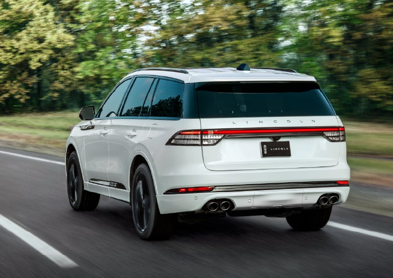A white 2026 Lincoln Aviator® SUV is being driven away down a road lined with colorful trees. | Napleton River Oaks Lincoln in Calumet City IL