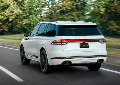 A white 2026 Lincoln Aviator® SUV is being driven away down a road lined with colorful trees. | Napleton River Oaks Lincoln in Calumet City IL