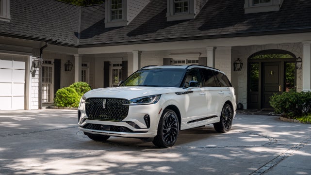 A white 2026 Lincoln Aviator® SUV is parked in the driveway of a luxury home. | Napleton River Oaks Lincoln in Calumet City IL