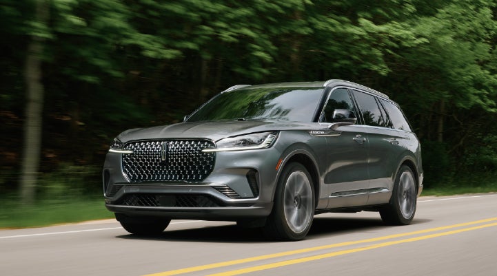A 2027 Lincoln Aviator® SUV is being driven down a road lined with trees. | Napleton River Oaks Lincoln in Calumet City IL